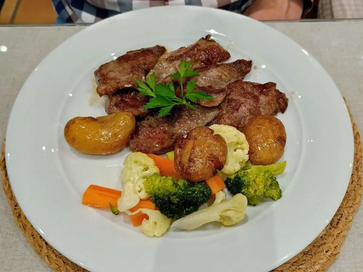Secreto ibérico a la plancha en lonchas con patatas, zanahoria, brócoli y coliflor en un plato blanco
