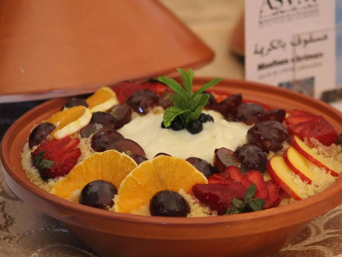 Cuenco de barro con cuscús dulce con nata, rodajas de naranja, fresas y moras