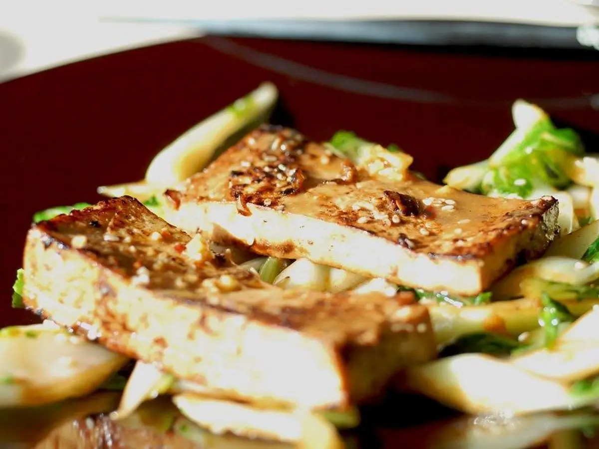 Lonchas de tofu glaseado y dorado con sésamo sobre pak choi salteado en un plato granate