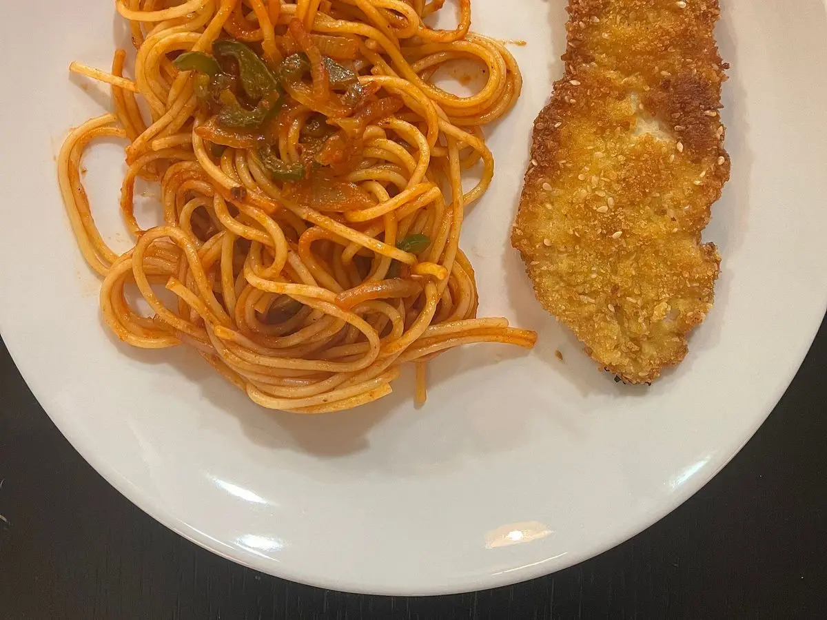 Plato blanco de espaguetis con salsa de tomate junto a un filete empanado dorado