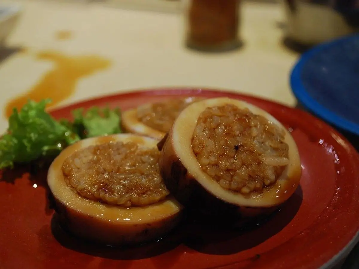 Calamar relleno de arroz cortado en rodajas sobre un plato rojo con brócoli