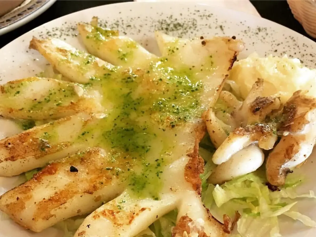 Cuerpos de sepia o calamar a la plancha con salsa verde de perejil sobre lechuga