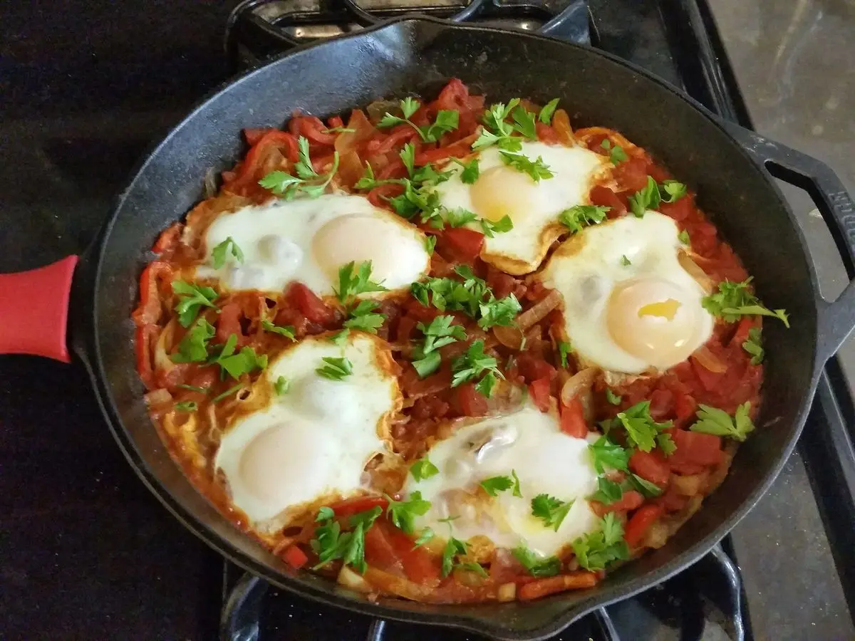 Sartén de hierro con shakshuka: salsa de tomate con huevos escalfados y perejil