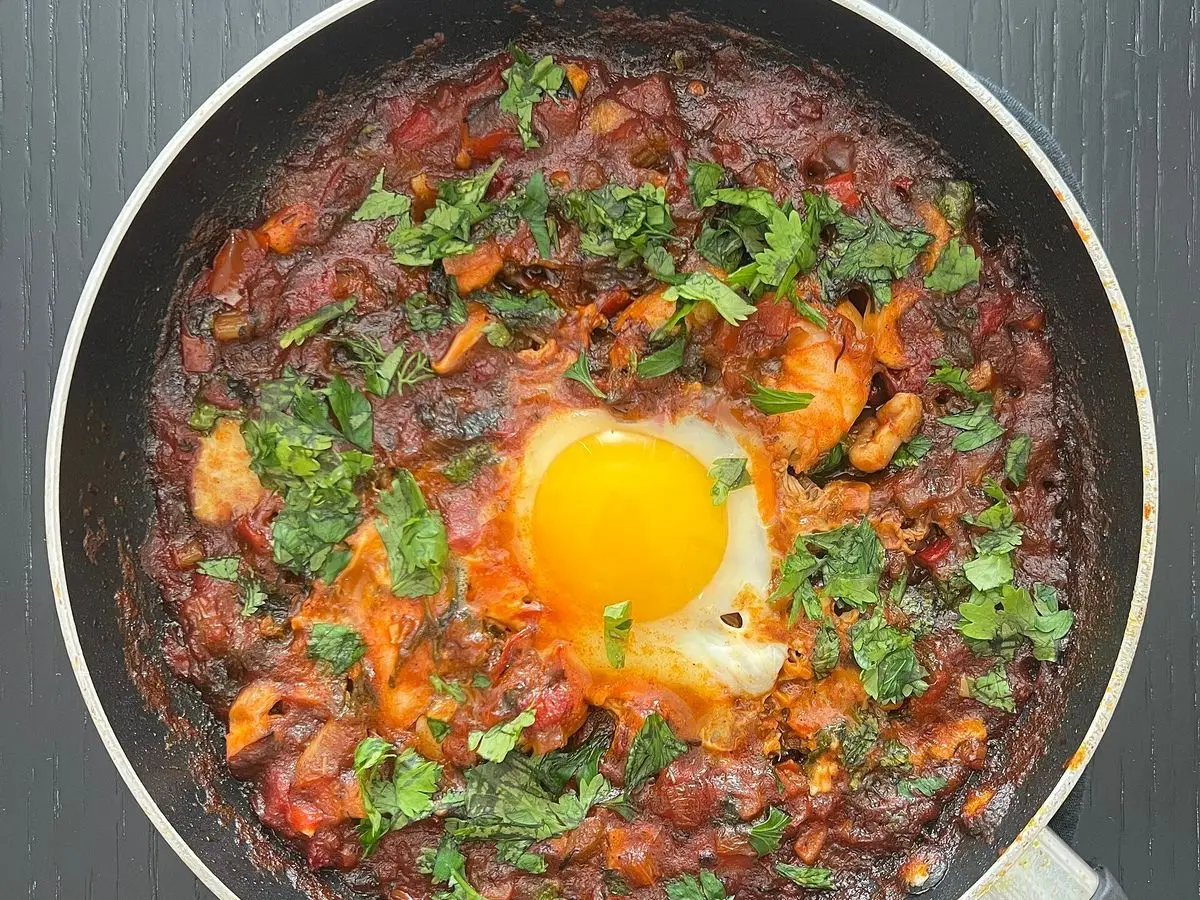 Sartén de shakshuka con un huevo frito en salsa espesa de tomate y verduras con cilantro picado por encima