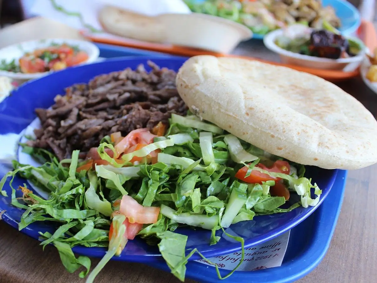 Plato azul con tiras de carne de shawarma, pan de pita, lechuga y tomate picado