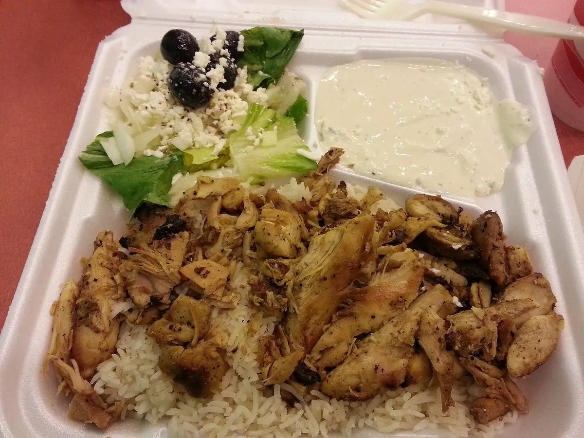 Pollo especiado sobre arroz con ensalada y salsa de yogur en una bandeja blanca