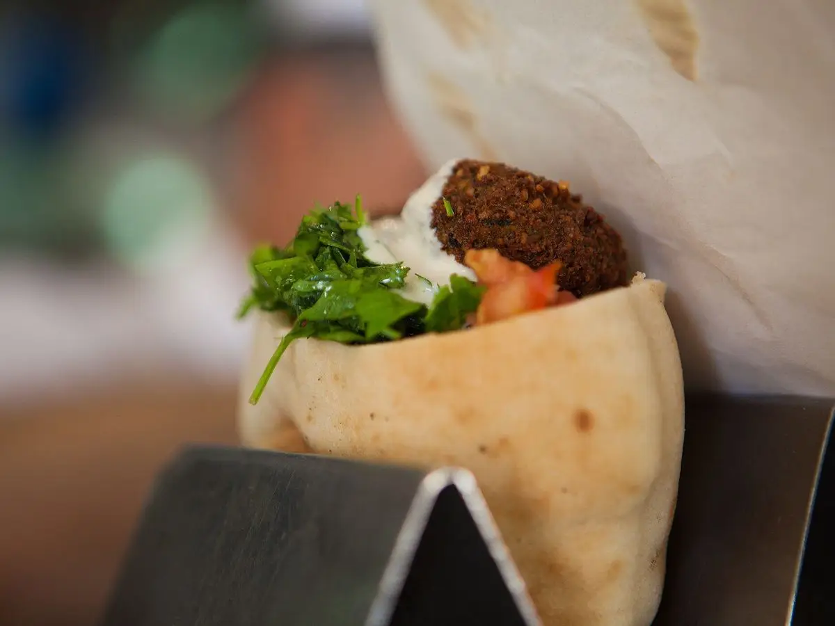 Pan de pita relleno de falafel, verduras frescas y hojas verdes, sostenido en un soporte