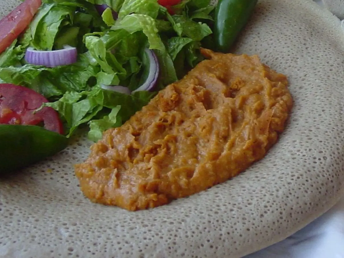 Plato con shiro etíope anaranjado y ensalada de lechuga, tomate y cebolla morada sobre injera