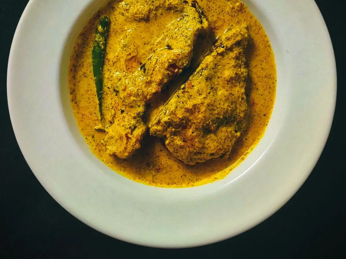 Plato blanco hondo con dos trozos de pescado en salsa cremosa de mostaza amarilla y una hoja verde