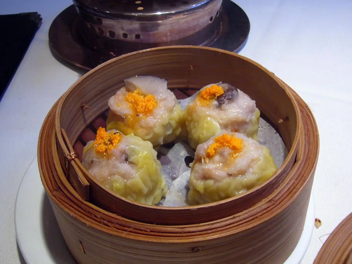 Cuatro shumai de cerdo al vapor con una pizca de zanahoria rallada en una vaporera de bambú