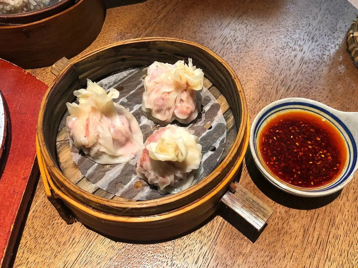Siu mai al vapor en una cesta de bambú junto a un cuenco de salsa de guindilla