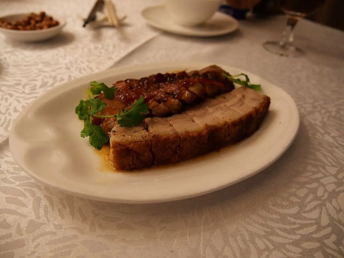 Panceta de cerdo asada con piel crujiente cortada en trozos sobre un plato blanco con verdura verde