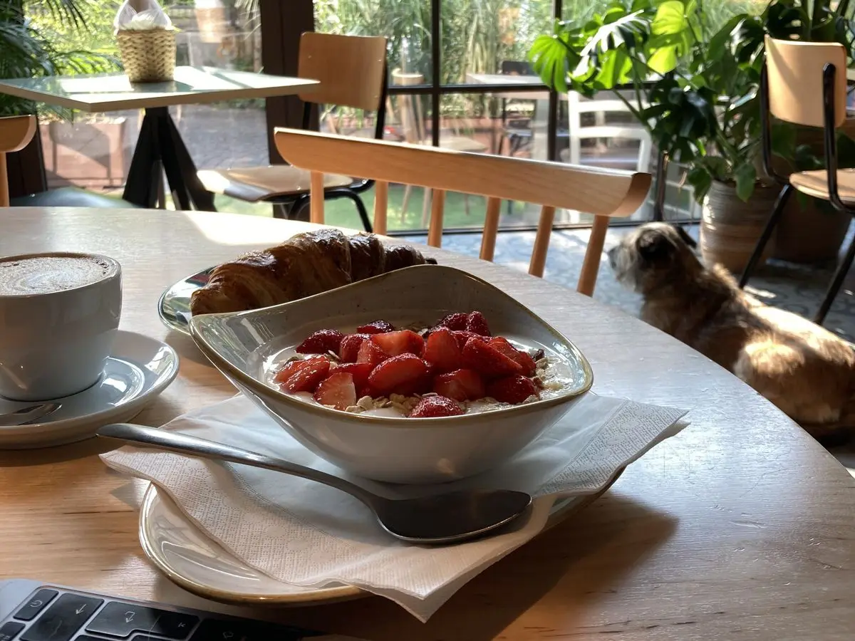 Cuenco de yogur con fresas troceadas y copos de cereal junto a un café y un cruasán