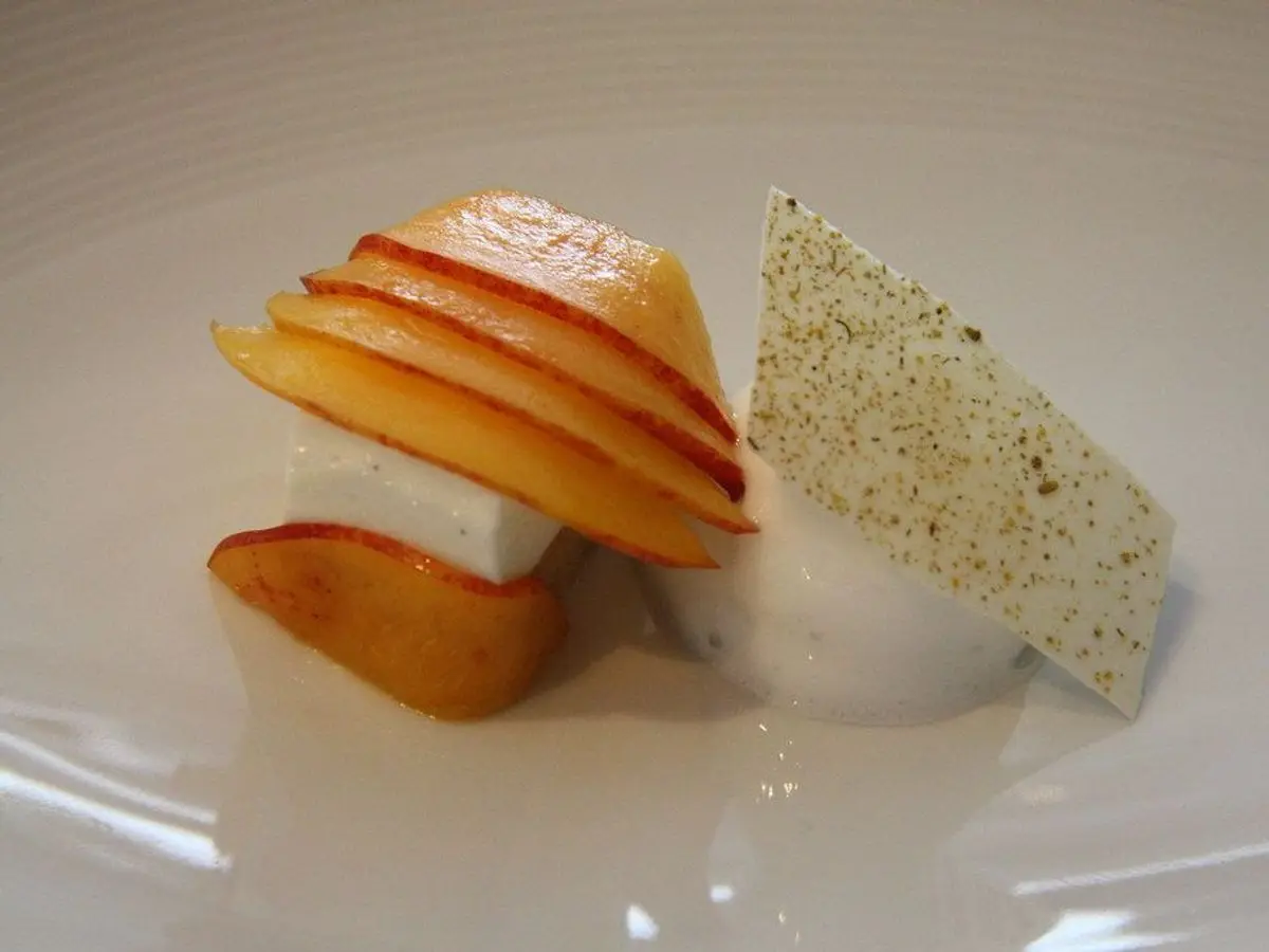 Láminas de nectarina con crema blanca y una teja crujiente de semillas en un plato blanco