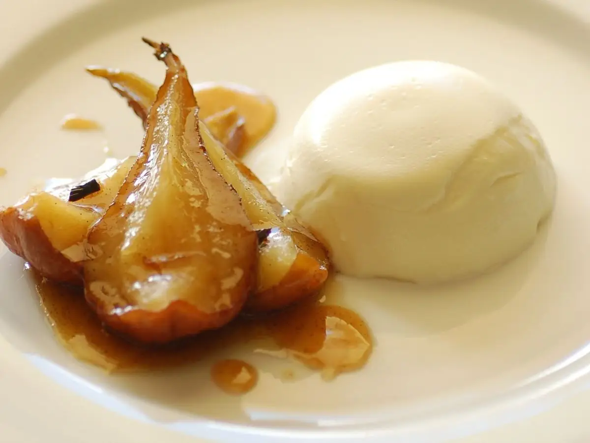 Pera asada y dorada junto a una crema blanca sobre un plato blanco