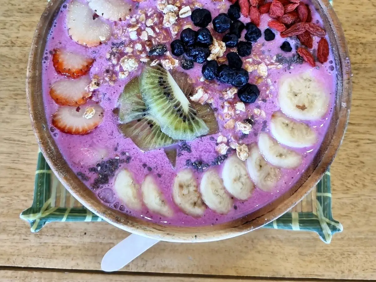 Bol de smoothie morado decorado con rodajas de plátano, fresa, kiwi, arándanos y frutos secos