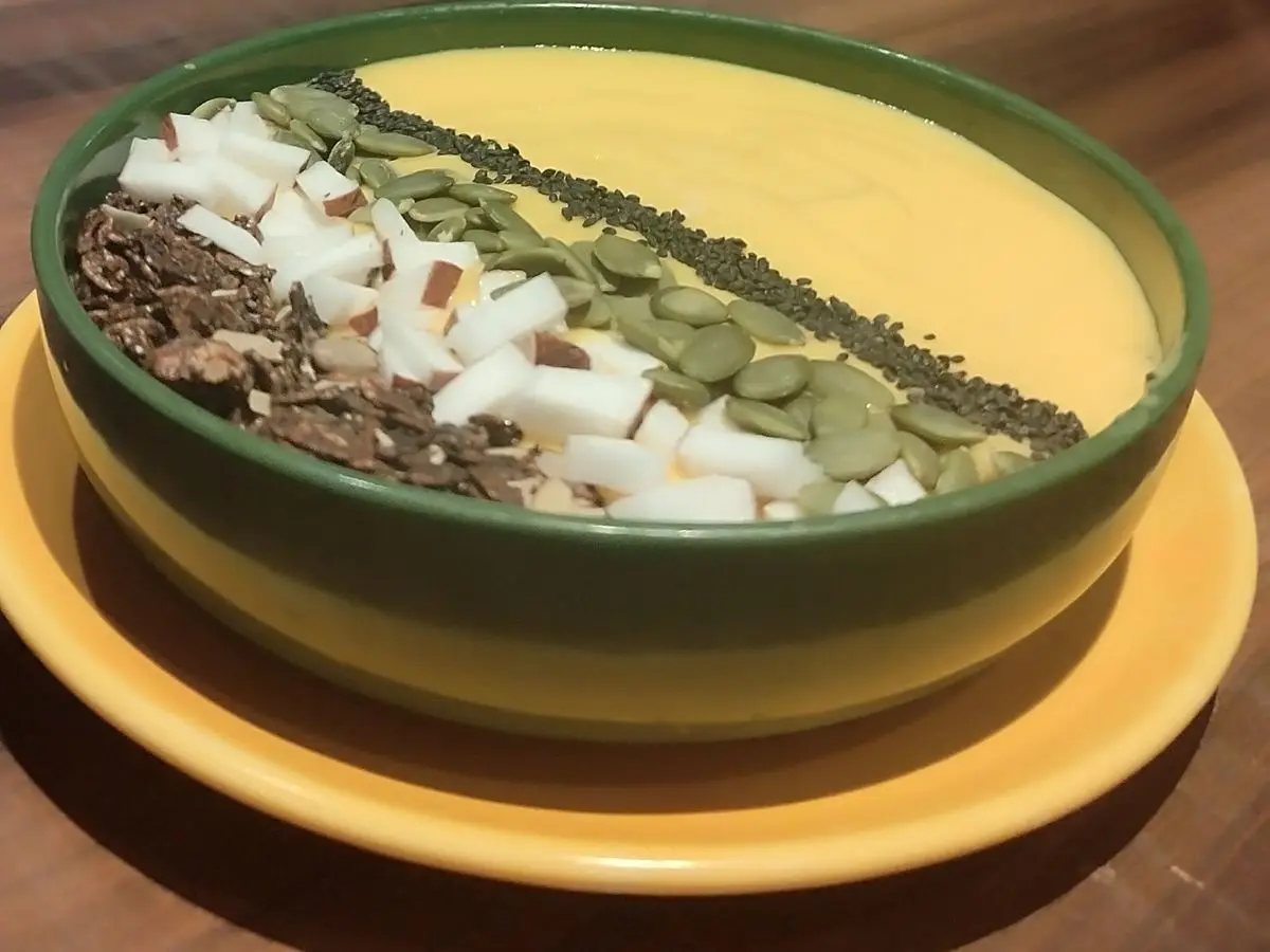 Cuenco verde con smoothie bowl amarillo de mango y coco, semillas y pipas por encima