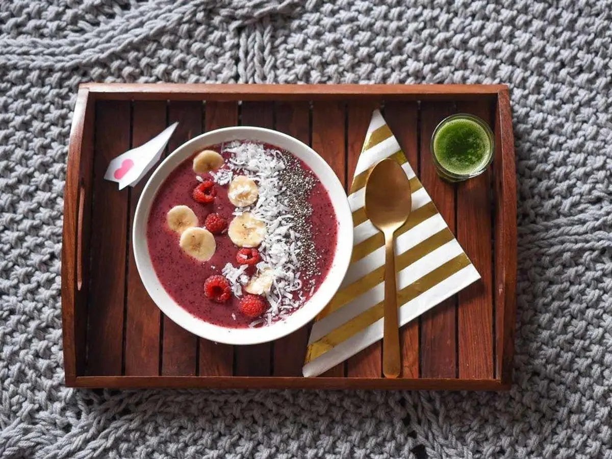 Cuenco de smoothie bowl rosa con rodajas de plátano y semillas sobre una bandeja de madera
