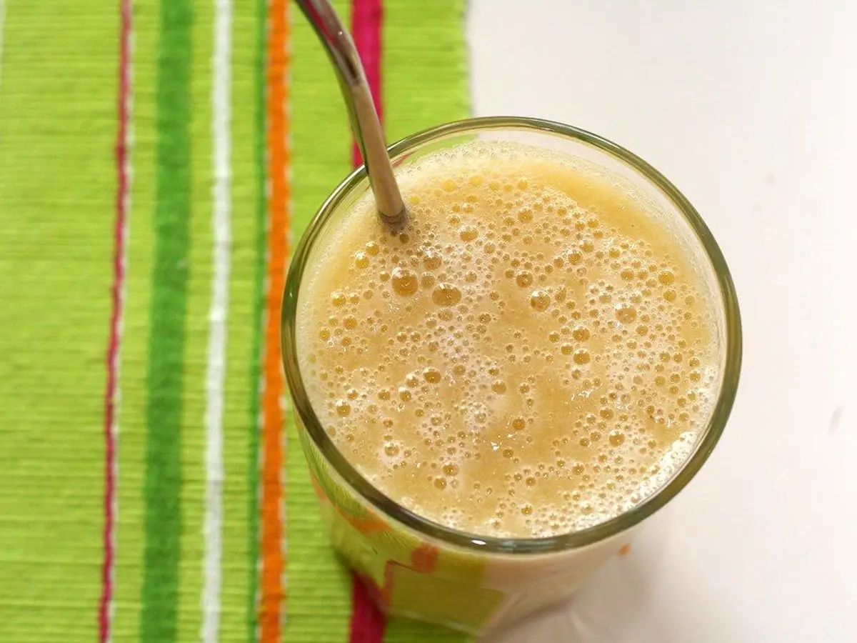 Vaso de batido espumoso amarillo anaranjado con una pajita sobre un mantel de rayas