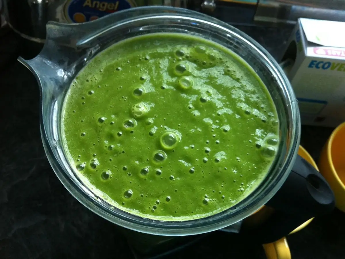 Jarra de cristal de batidora llena de batido verde intenso y espumoso