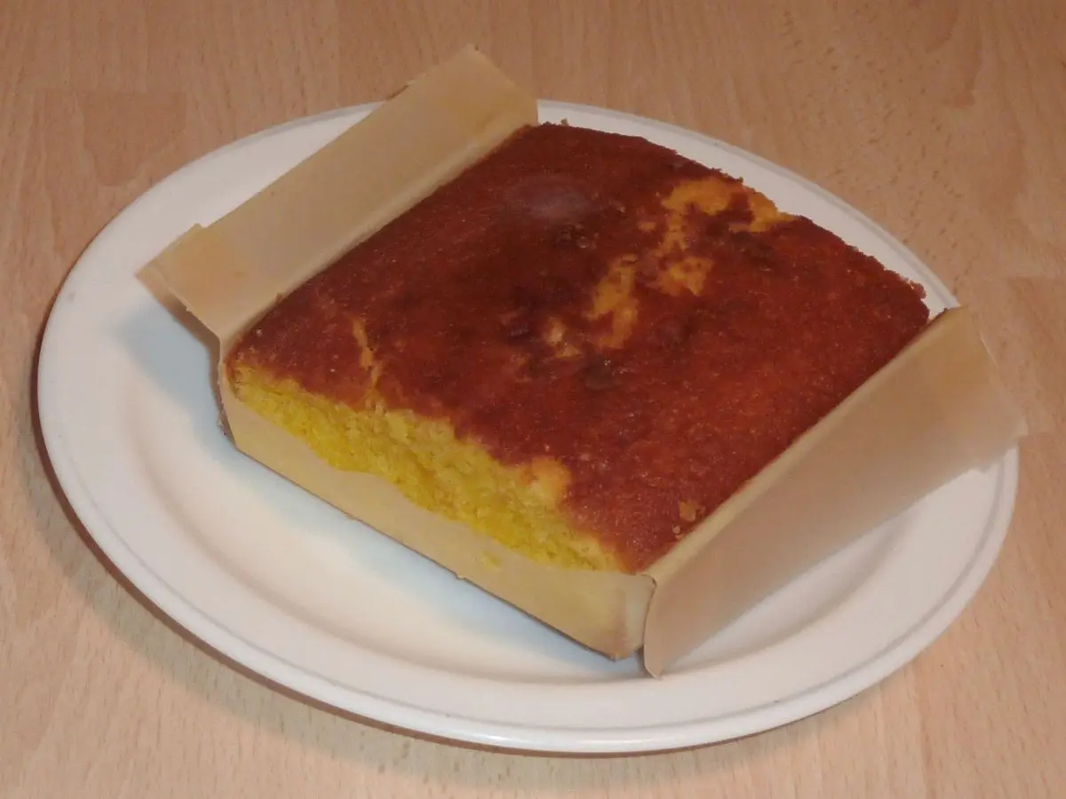 Sobao pasiego, bizcocho de mantequilla dorado en su papel, servido sobre un plato blanco
