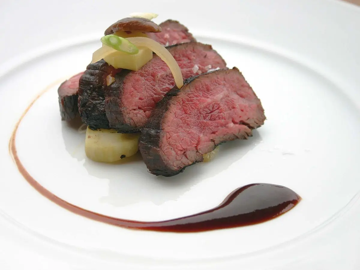 Lonchas de falda de ternera asada con cebolla y patata sobre plato blanco con salsa oscura