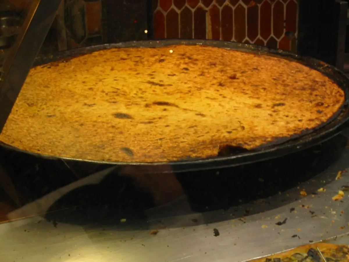 Gran sartén redonda con una socca de harina de garbanzo dorada recién salida del horno