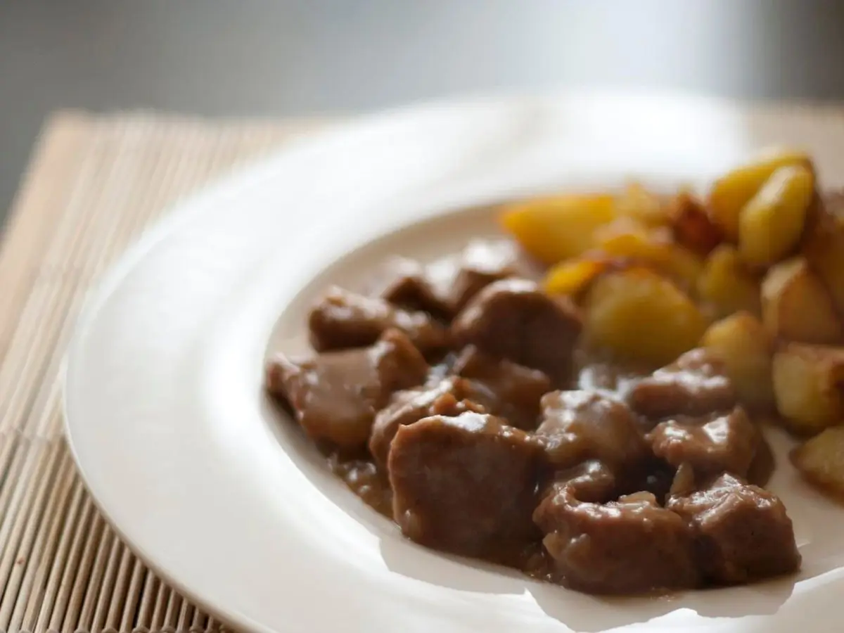 Plato blanco con trozos de carne guisada en su salsa y patatas doradas