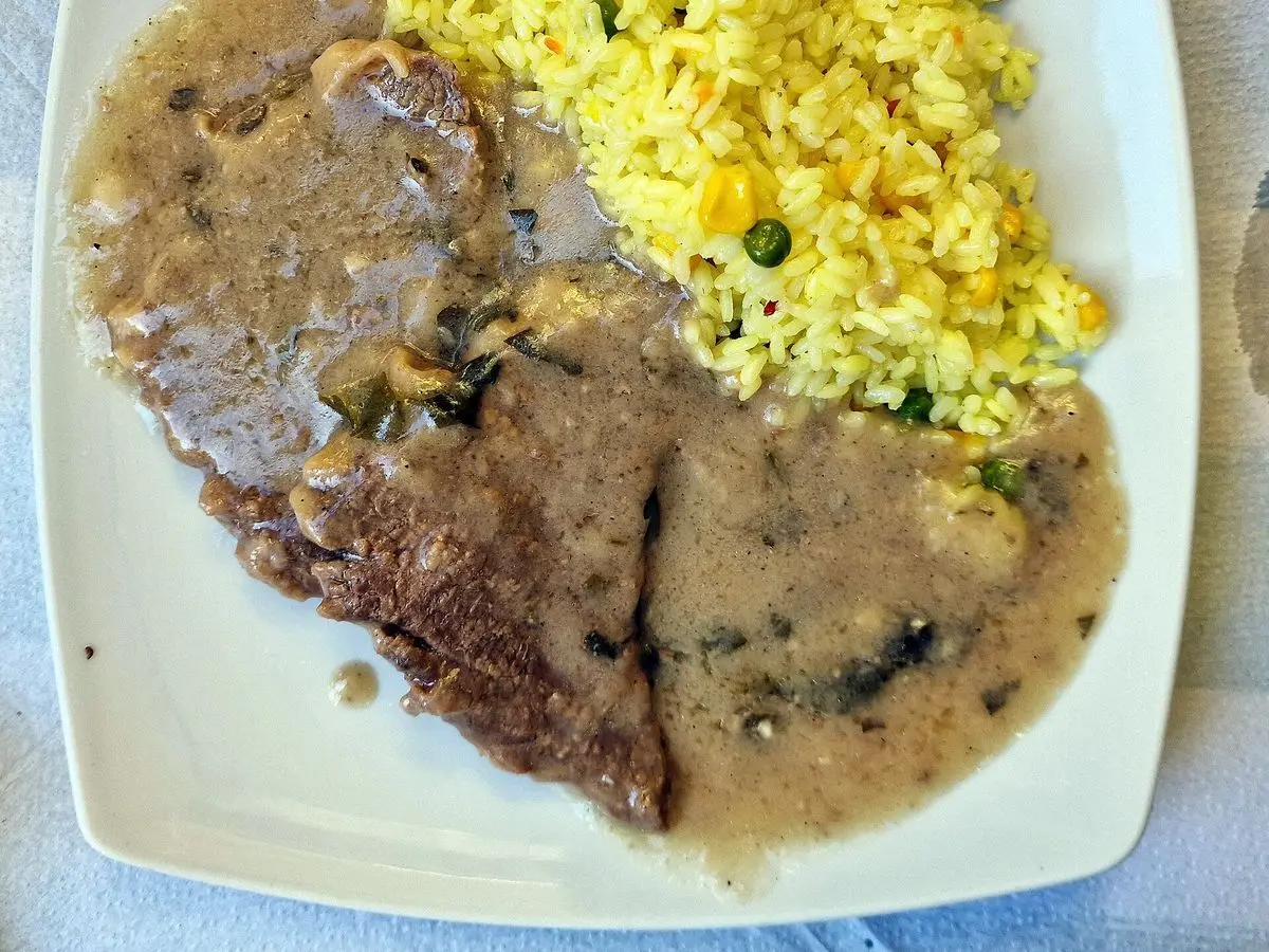 Plato ovalado con filete de ternera en salsa cremosa de ajo y arroz amarillo con guisantes