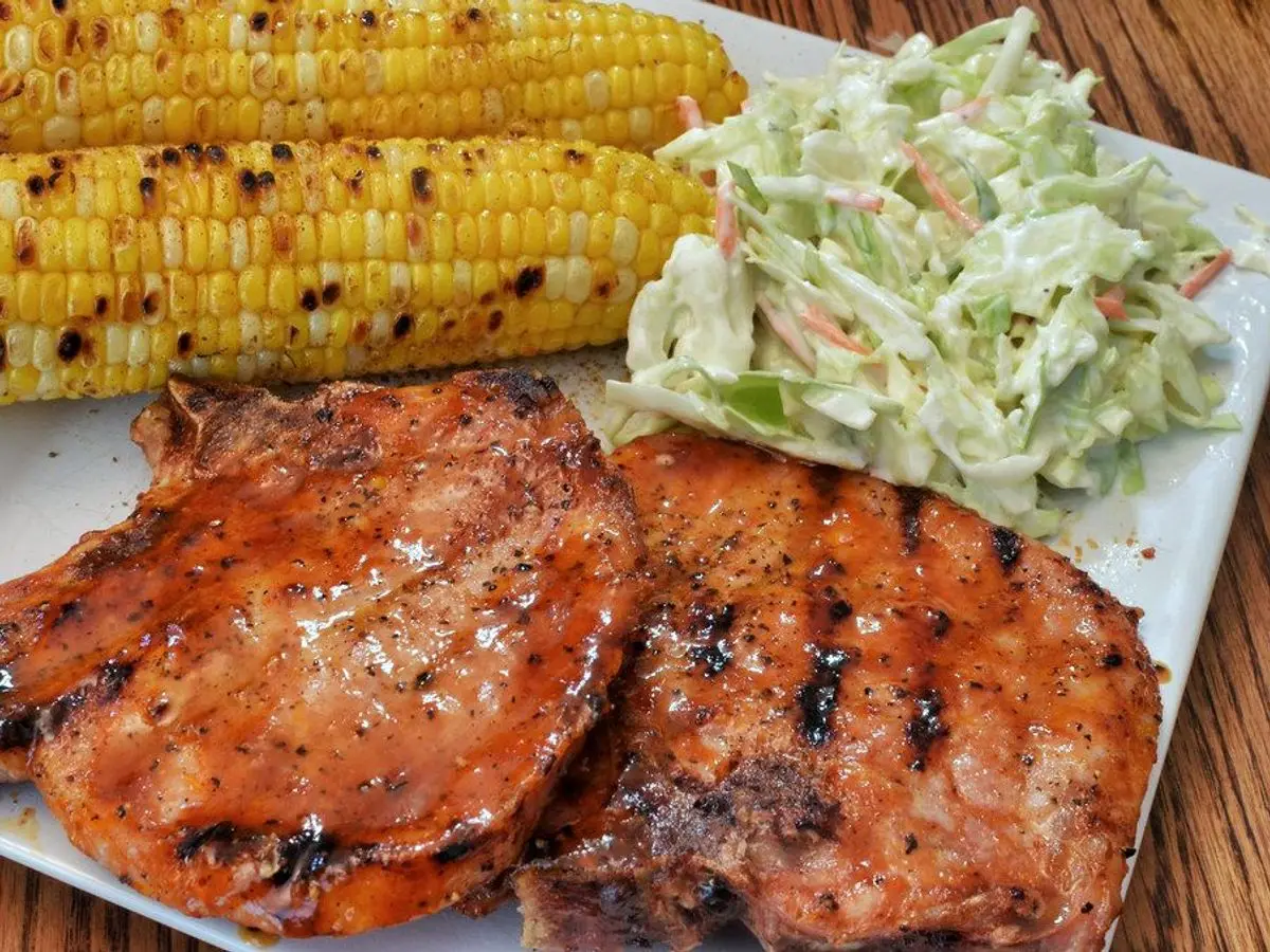 Chuletas de cerdo a la parrilla con mazorcas de maíz asadas y ensalada de col