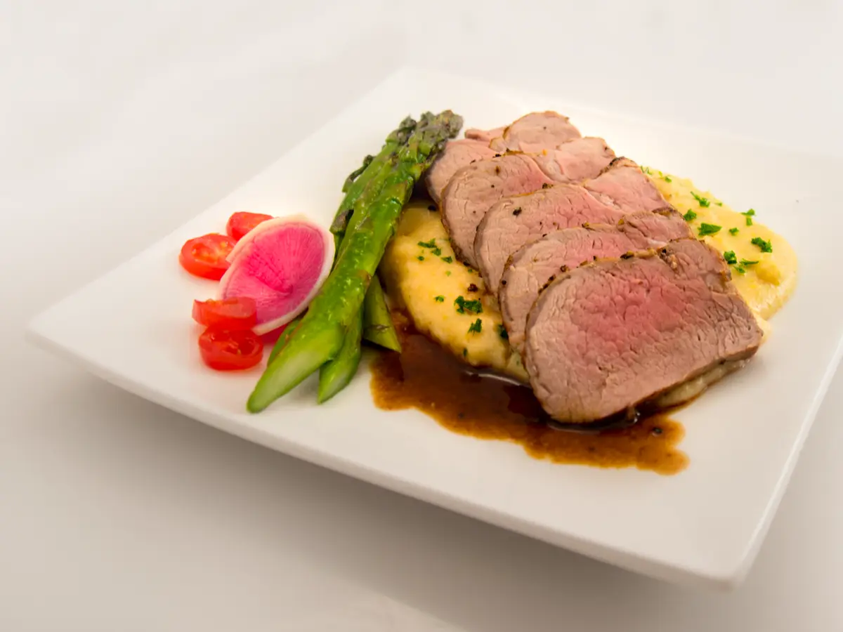 Lonchas de solomillo de cerdo con puré cremoso y espárragos verdes en un plato cuadrado