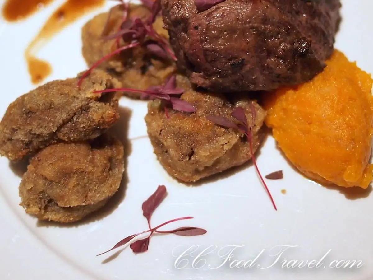 Medallón de solomillo de cerdo con puré de calabaza anaranjado y salsa sobre un plato blanco