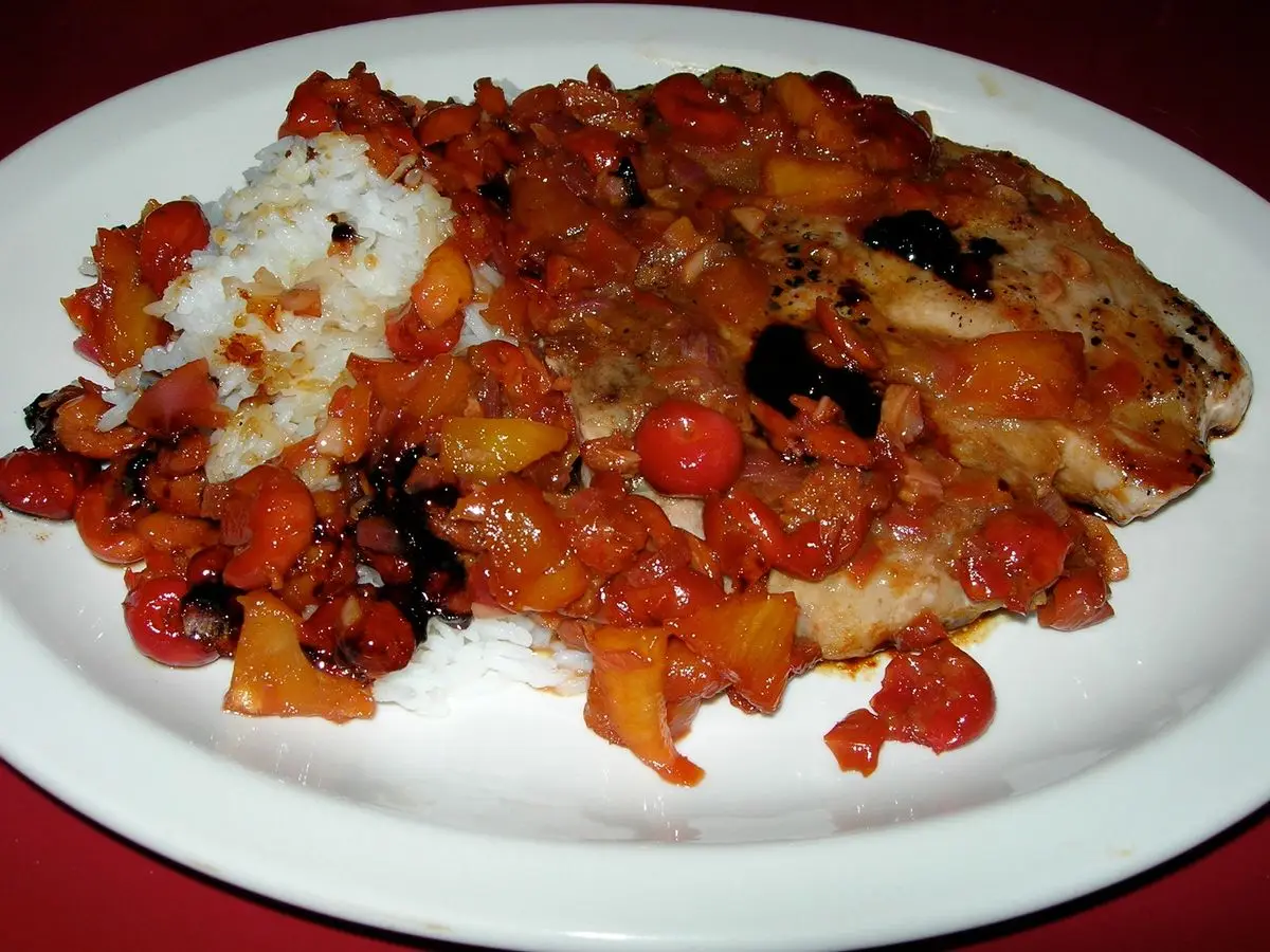 Filete de cerdo con arroz y salsa roja agridulce de cerezas en un plato blanco