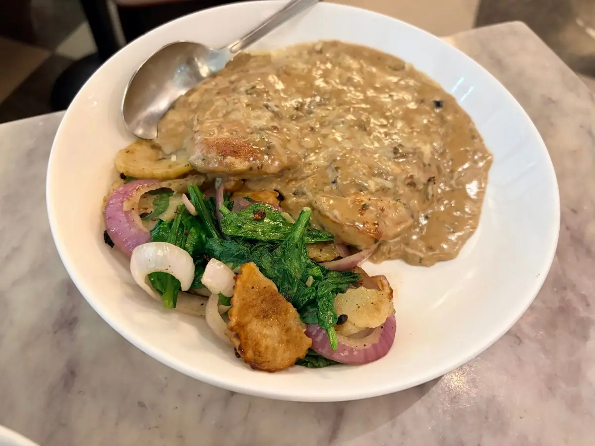 Filete de carne dorado cubierto de salsa cremosa de champiñones, con espinacas y cebolla salteadas