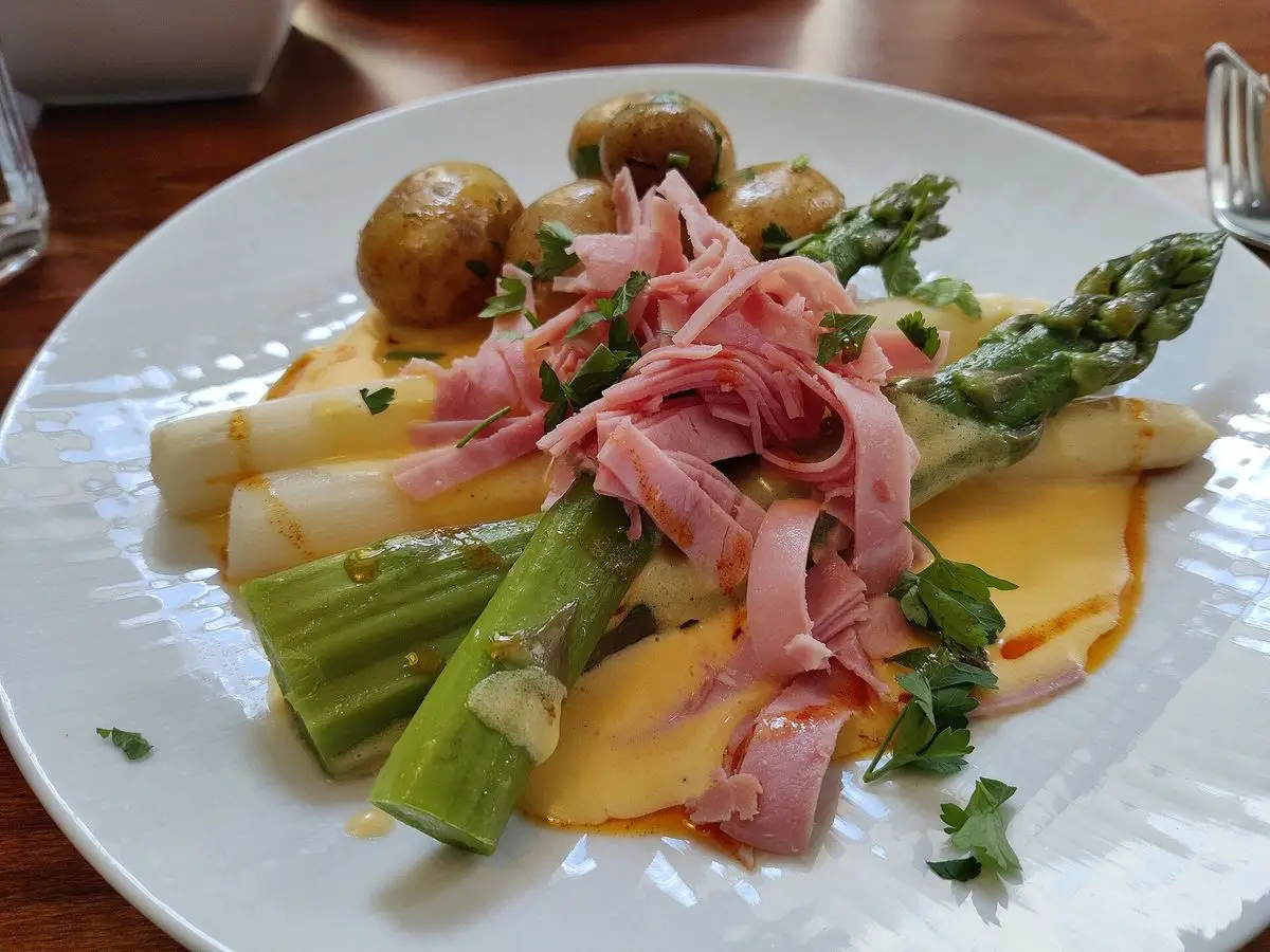 Plato blanco con espárragos blancos y verdes, patatas nuevas, lonchas de jamón y salsa cremosa