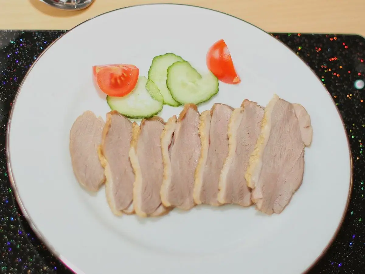 Lonchas de pechuga de pavo asada en un plato blanco con rodajas de pepino y tomate