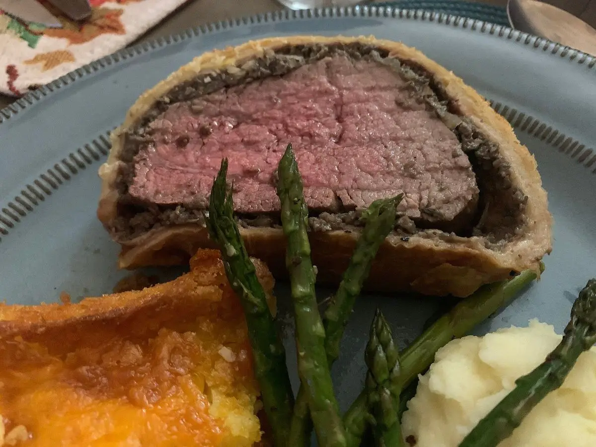 Rodaja de solomillo Wellington con hojaldre dorado, espárragos verdes y puré de patata en un plato