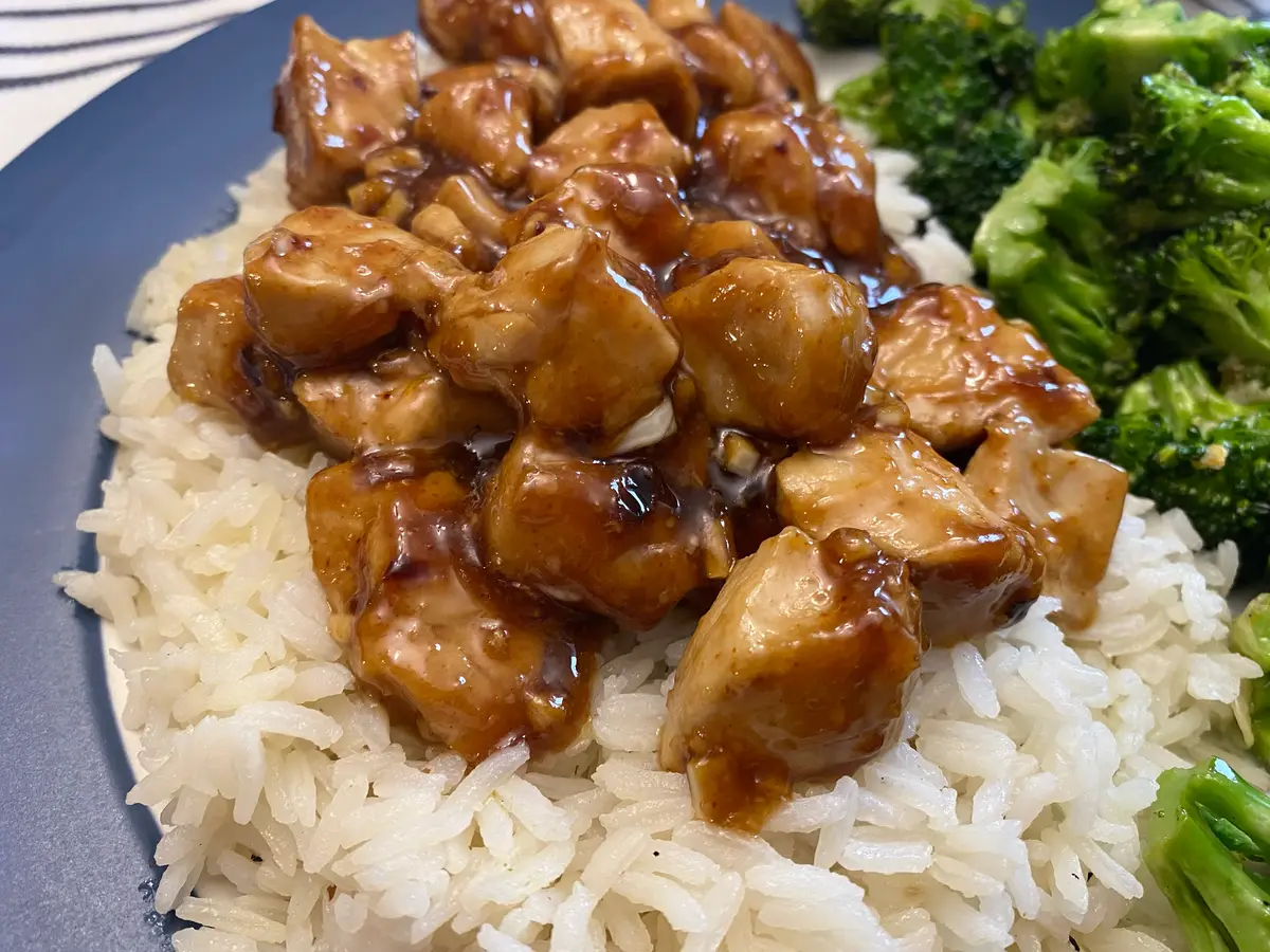 Trozos de pollo en salsa oscura sobre arroz blanco con brócoli al lado en un plato azul