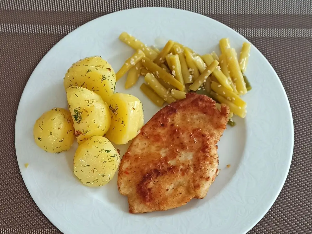Filete de pollo dorado con patatas nuevas pequeñas y judías verdes planas en un plato blanco