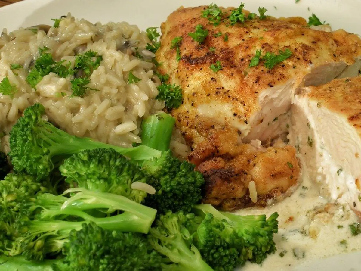 Pechuga de pollo dorada rellena con brócoli y arroz cremoso en un plato blanco