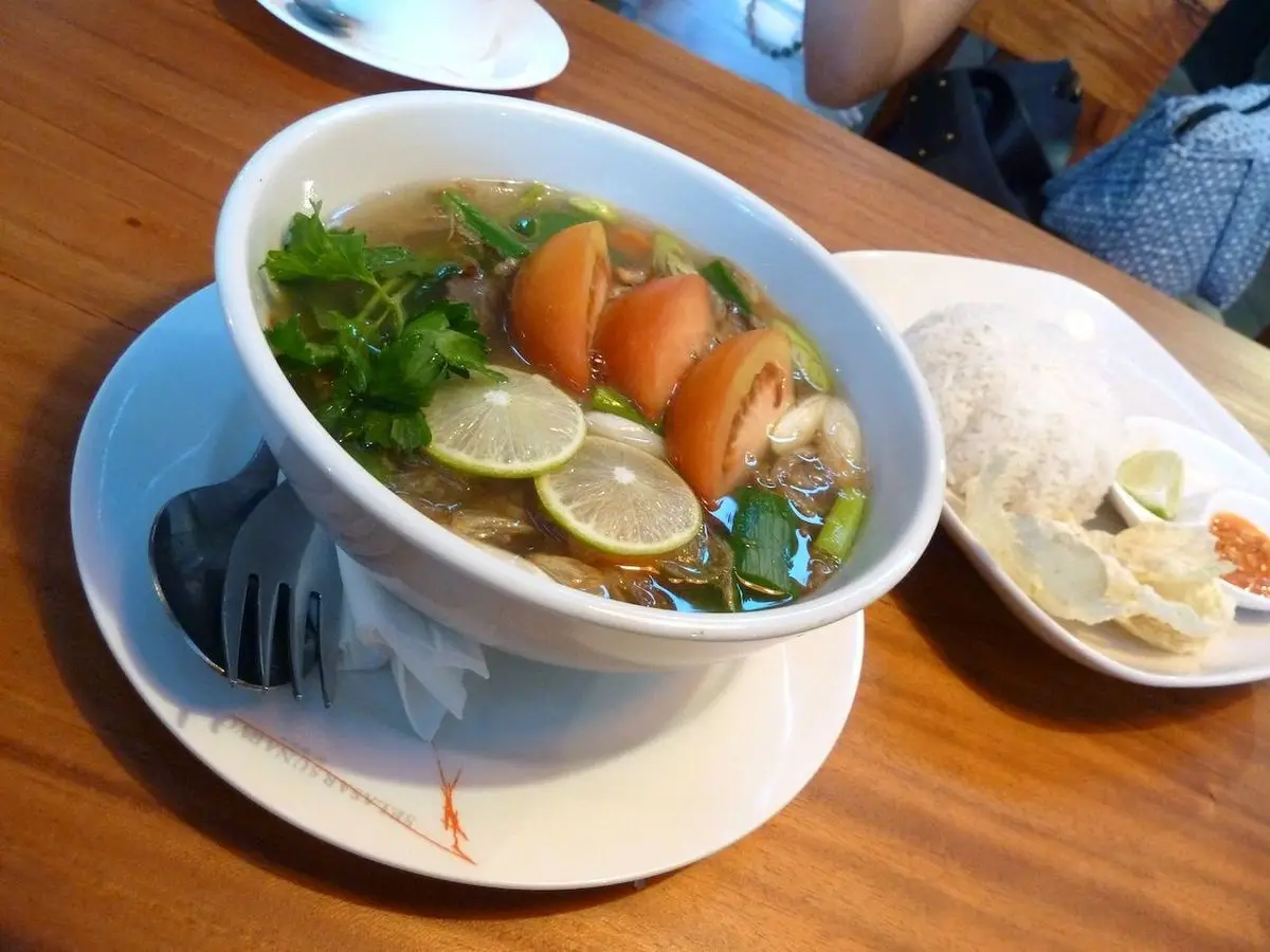 Cuenco de sopa de rabo con zanahoria, rodajas de lima y cebolleta, con arroz al lado