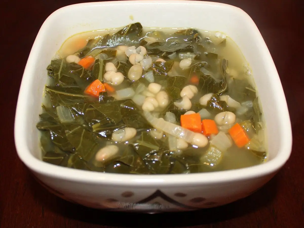 Cuenco cuadrado blanco de sopa de alubias blancas con hojas verdes y zanahoria en dados