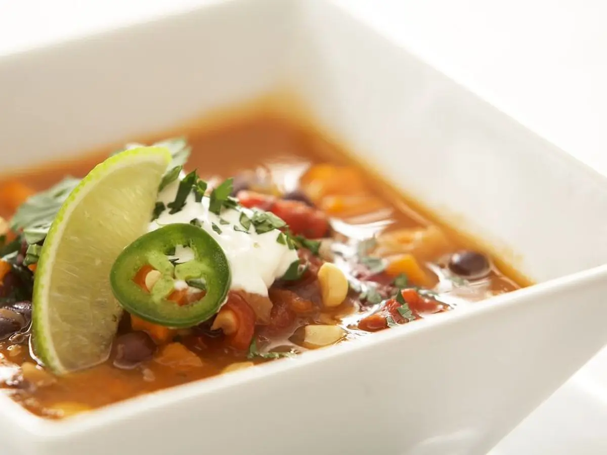 Cuenco blanco de sopa de alubias negras y verduras con rodaja de lima, jalapeño y crema