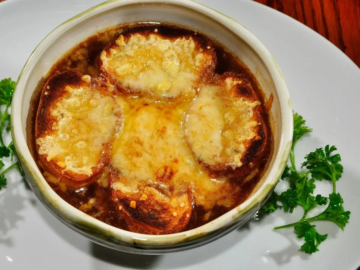 Cazuela de sopa de cebolla gratinada con queso fundido dorado sobre un plato con perejil