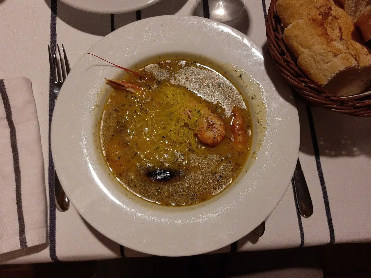 Plato hondo de sopa de pescado dorada con gamba y mejillones sobre un mantel de rayas