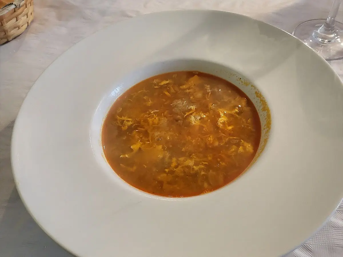 Plato hondo blanco con sopa de pan rojiza de pimentón y ajo con hebras de huevo cuajado