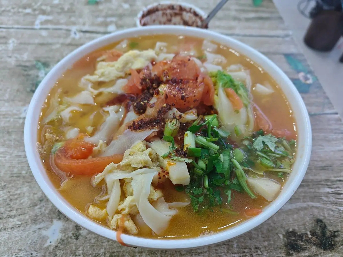 Cuenco de sopa de fideos con tomate, huevo y cebolleta picada sobre una mesa de madera