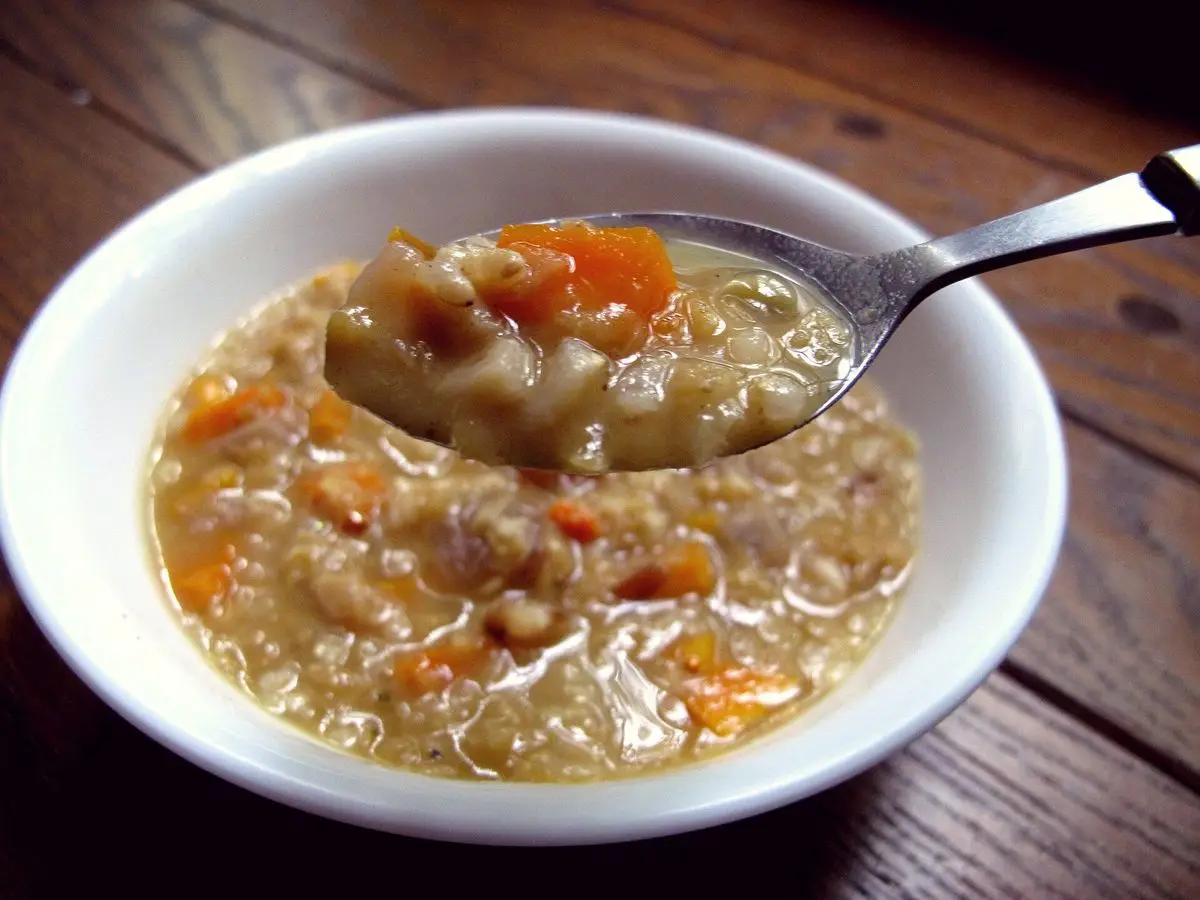 Cuenco blanco de sopa de lentejas con zanahoria y cuchara sobre mesa de madera