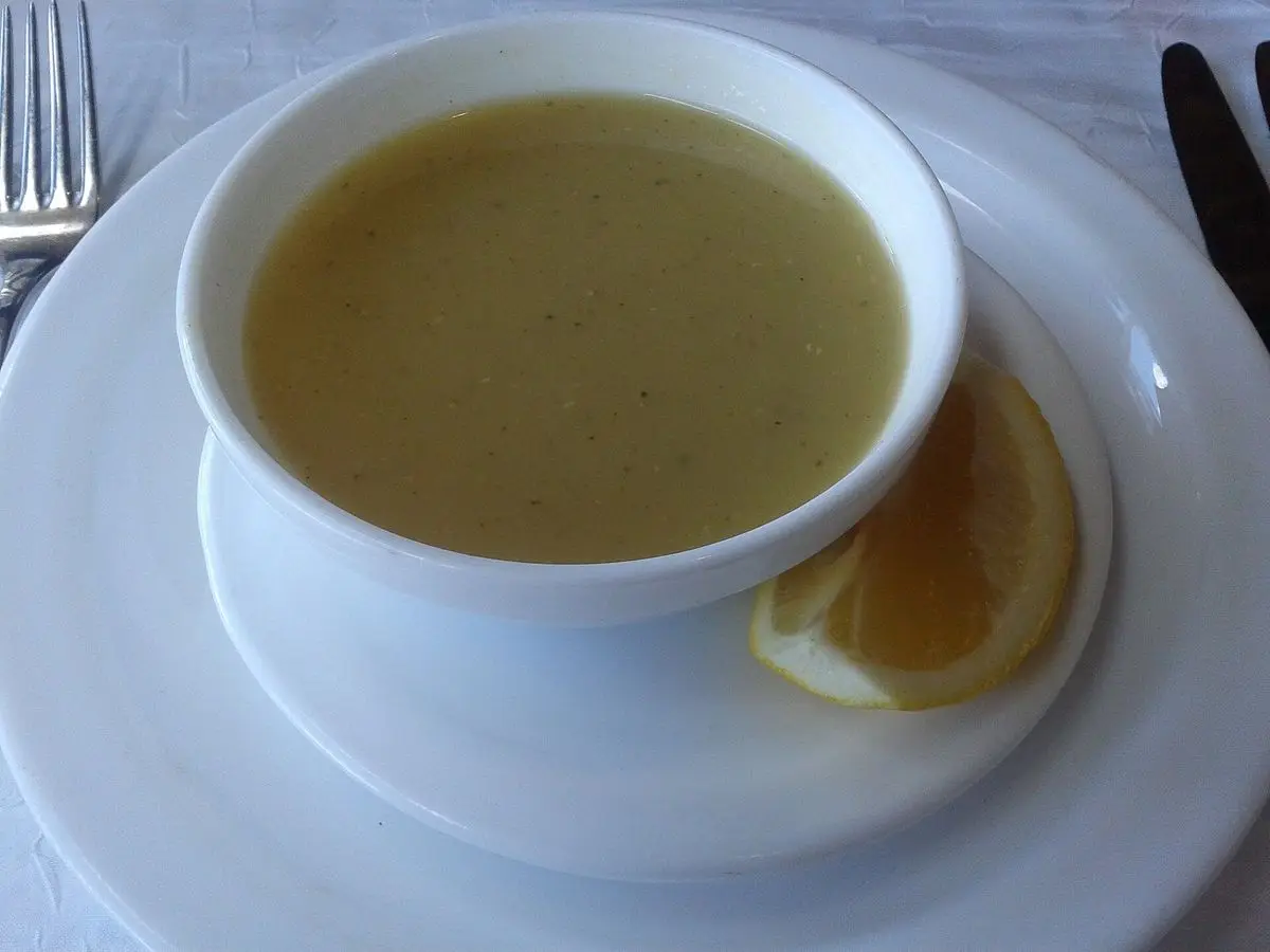 Taza blanca de sopa cremosa de lentejas con un gajo de limón sobre un plato