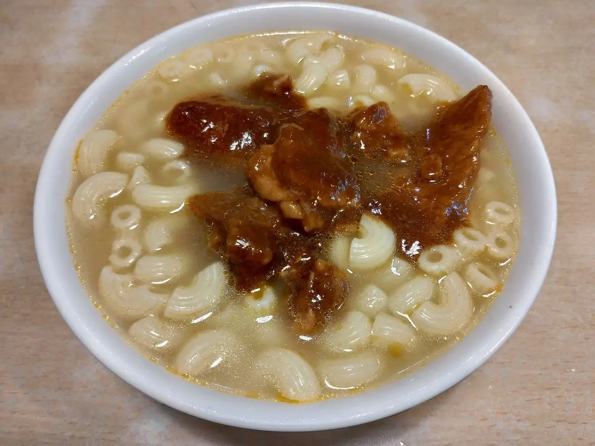 Cuenco blanco de sopa de macarrones en caldo claro con trozos de carne asada por encima